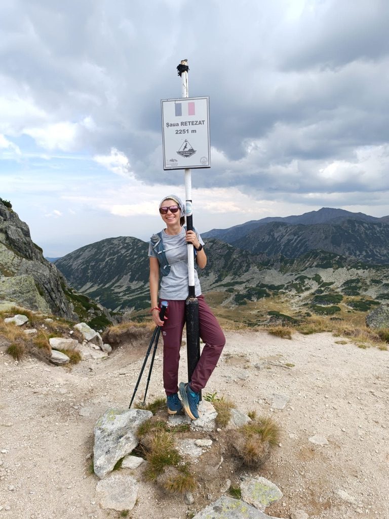 Anca standing at Saua Retezat summit marker at 2251 metres in the Romanian Carpathians