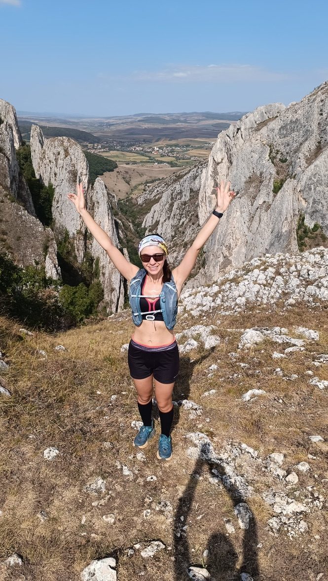 Anca jumping with arms raised between rocky canyon walls in Romania's Turda Gorge, triumphant and free