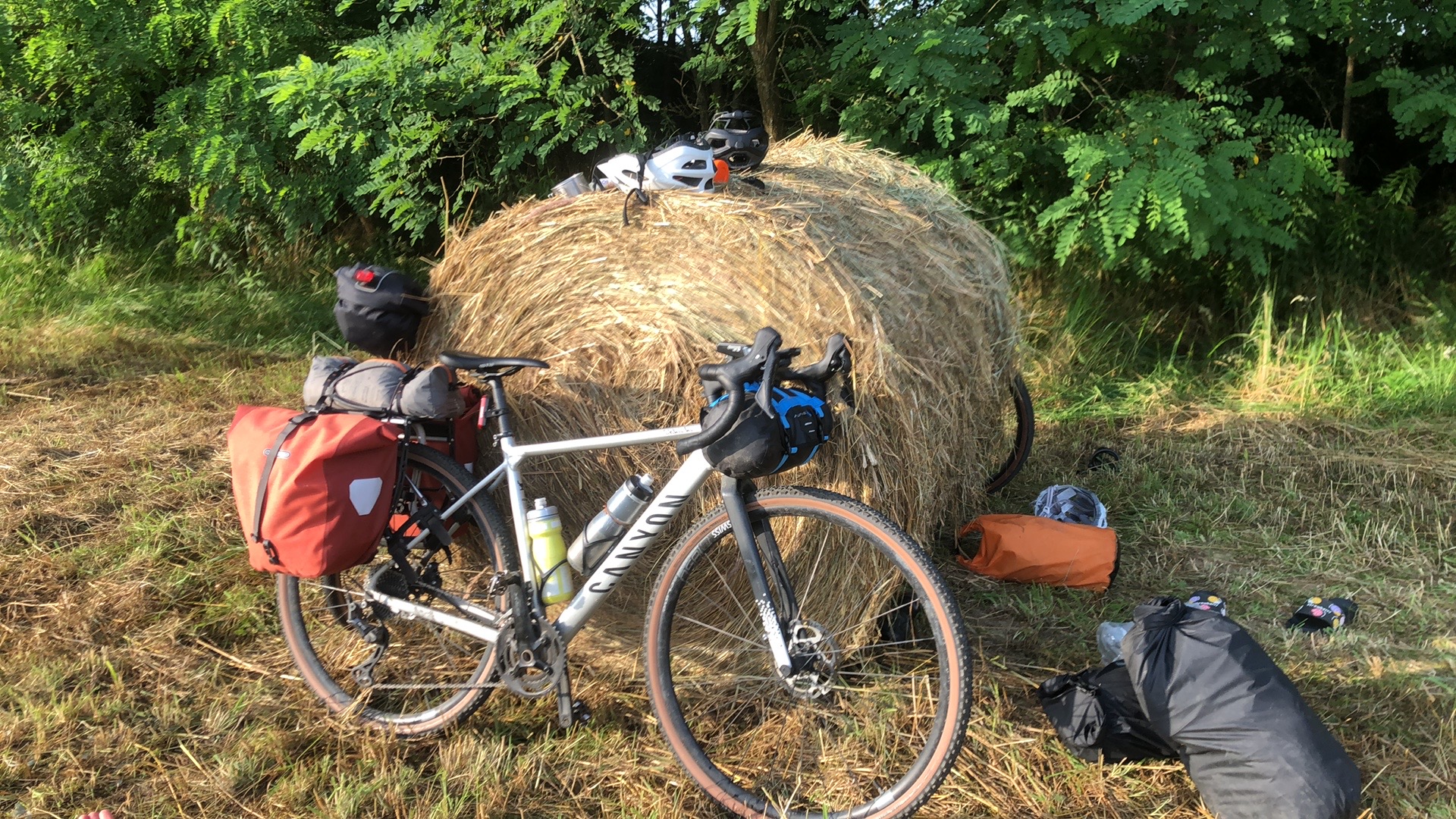 Loaded touring bike leaning against a giant hay bale in a golden field at sunset, Serbia