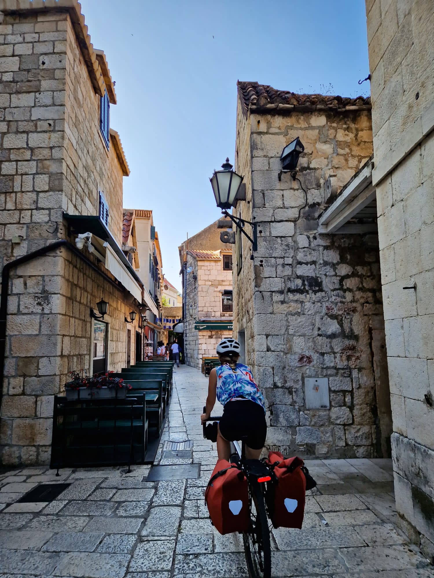 Cyclist with red panniers riding through a narrow stone street into Dubrovnik's old town