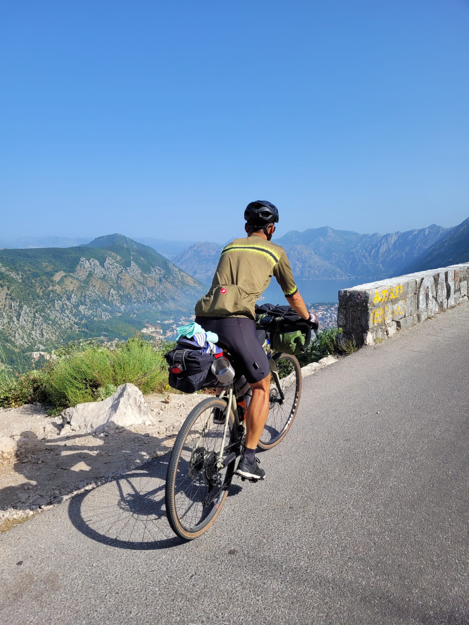 Cyclist with loaded panniers on a coastal mountain road overlooking a bay, Croatia