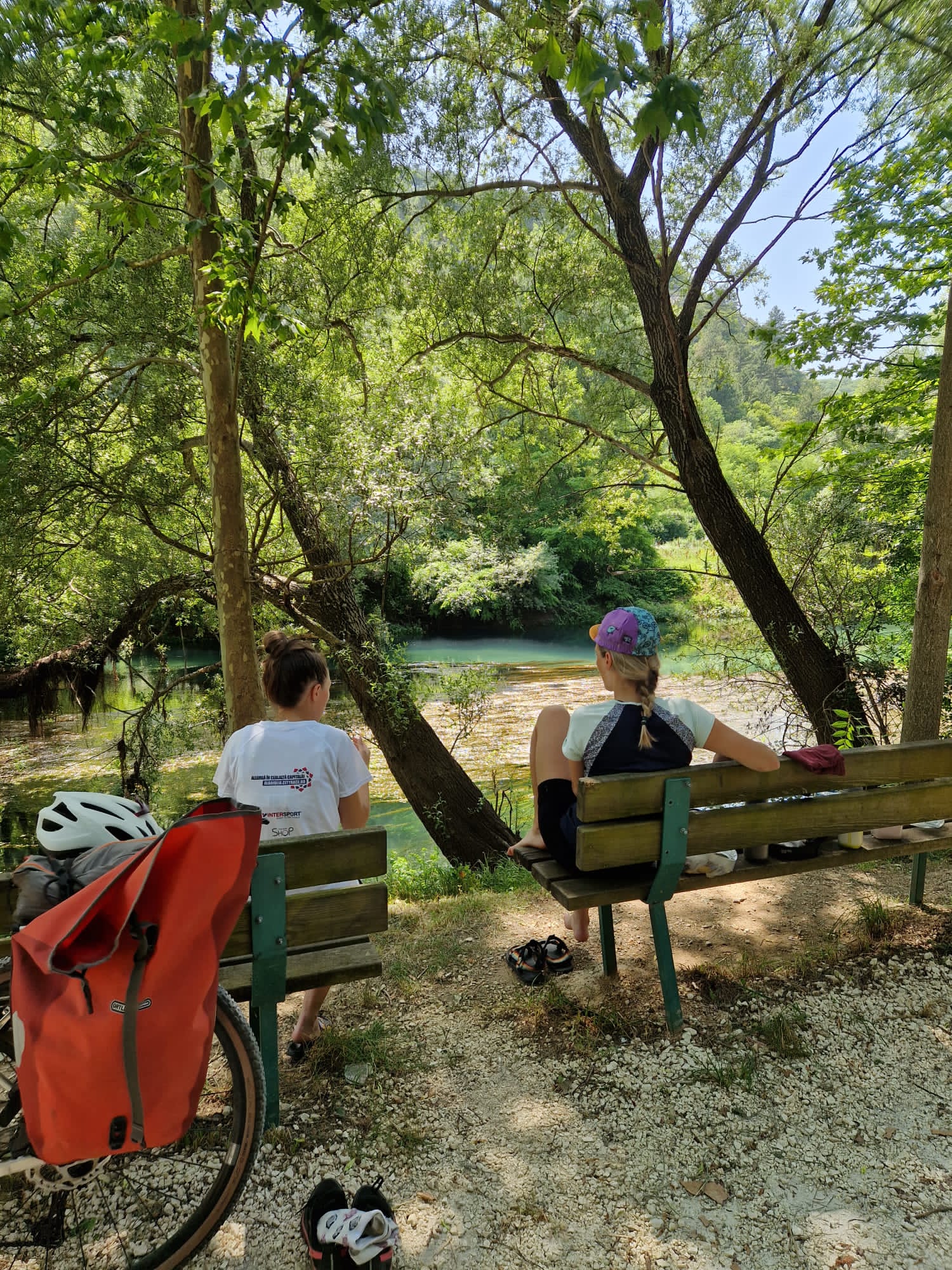 Two cyclists resting on benches in the shade by a river, hiding from the midday sun, Bosnia