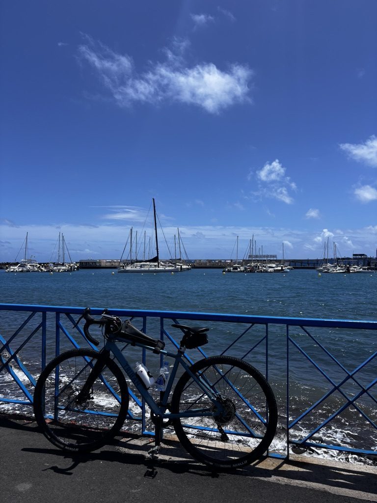 Anca cycling along a coastal Tenerife road, sea below, cliffs above, the bike and the horizon