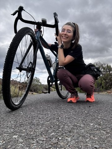 Anca on the bike on a Tenerife road — grinning, moving, the coast and sky open behind her