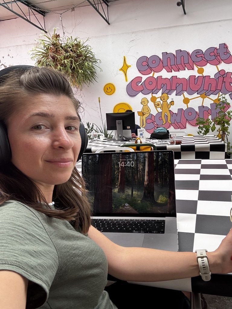 Anca working at laptop in a cowork space with 'Connect Community Work' mural on the wall