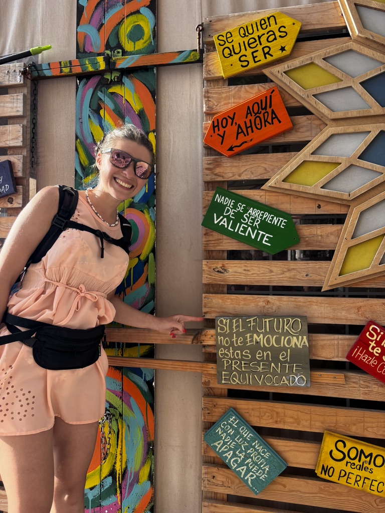 Anca pointing at a colourful sign that reads 'Nadie se arrepiente de ser valiente' — nobody regrets being brave