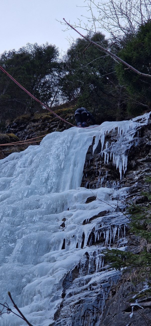 Climber at the very top of the frozen waterfall, pulling themselves over the final edge
