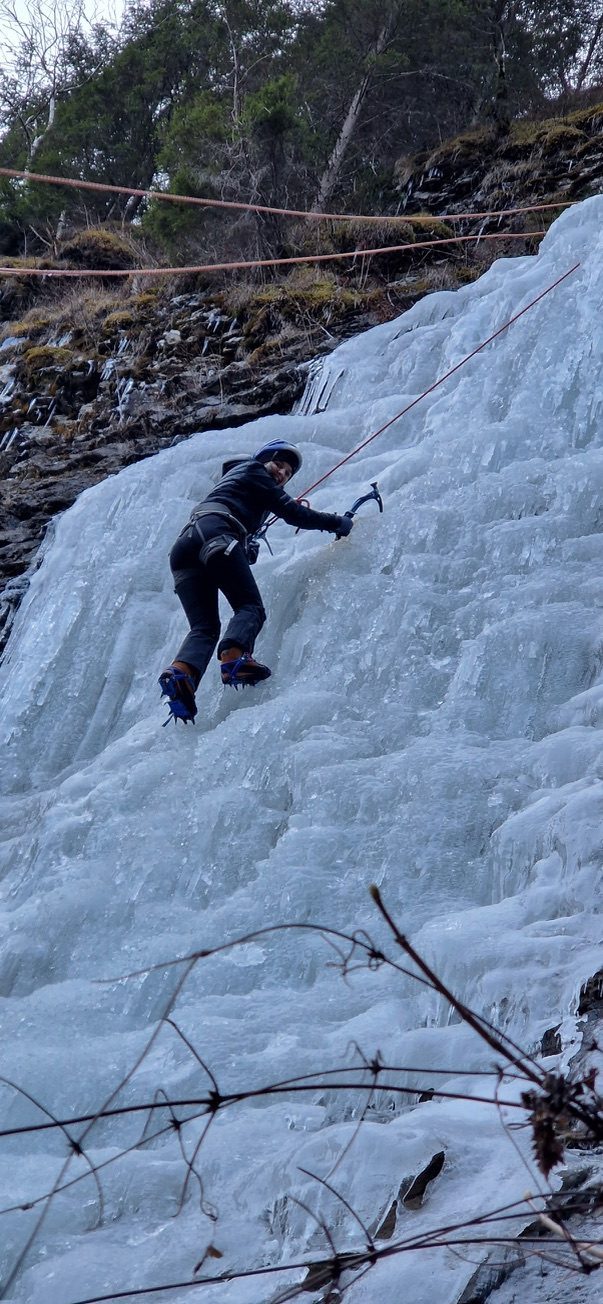Climber in black on the upper section of the frozen waterfall, above the curtain of icicles