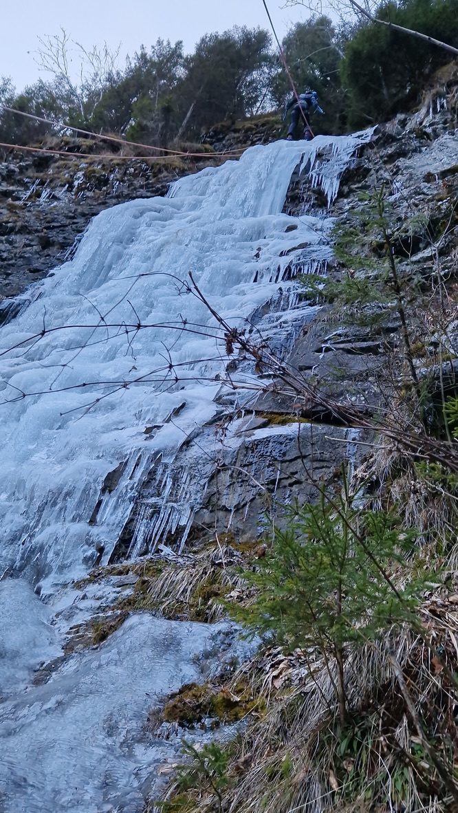 Anca on the frozen waterfall face, smiling toward the camera, ice axes and crampons in use