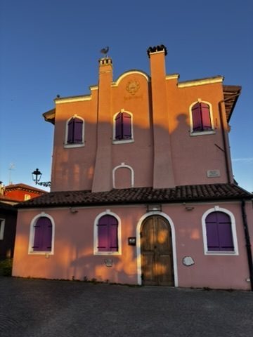Narrow street in Caorle old town lined with coloured painted houses — ochre, terracotta, faded blue — under warm Italian light