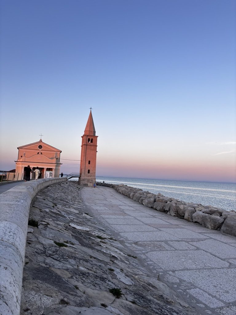 Sunset over Caorle lagoon, Italy — sky deep orange and pink, belltower silhouetted
