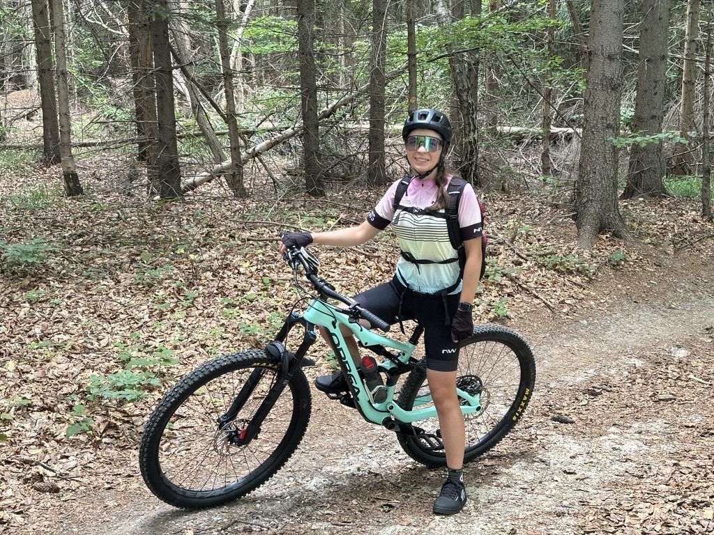 Anca standing with the Orbea in Fagăt forest, smiling, autumn leaves on forest floor