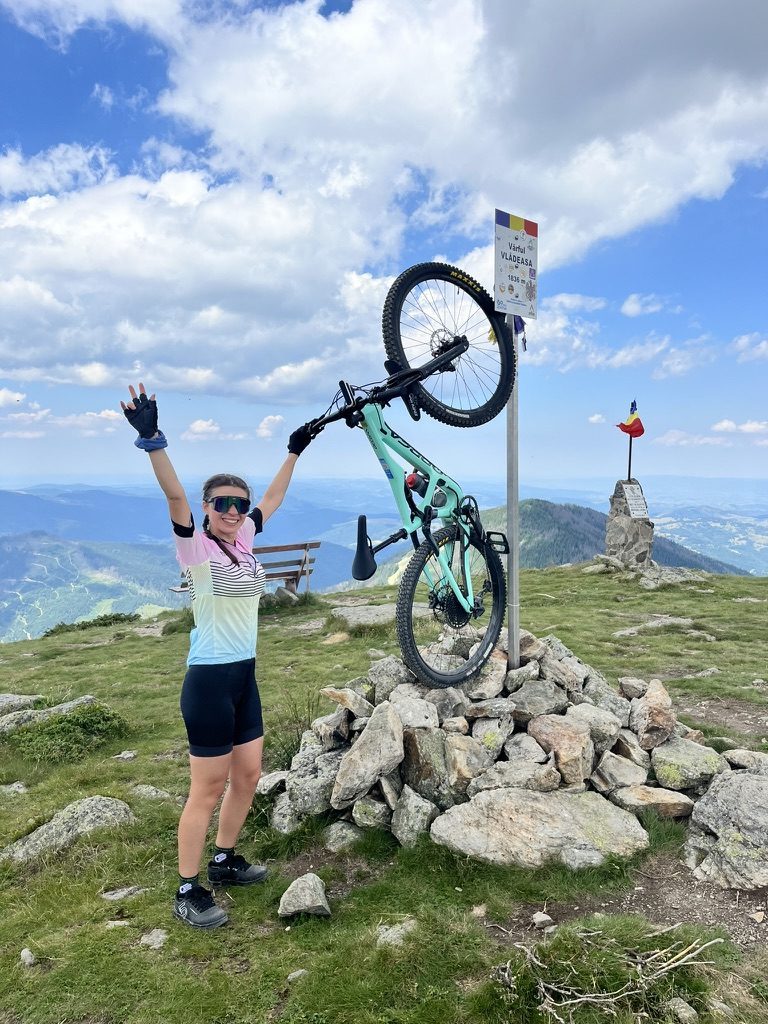 Anca at Vlădeasa summit, arms raised, holding Orbea