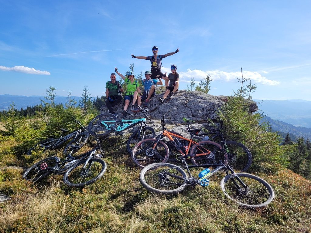 Group of 5 cyclists celebrating on a rocky summit at Finișel, bikes laid out, Apuseni mountains behind