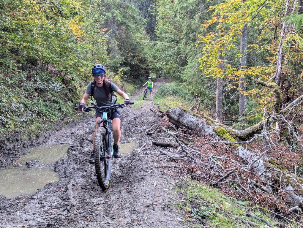 Anca and a friend riding through deep mud on a forest trail, autumn leaves, puddles across the trail