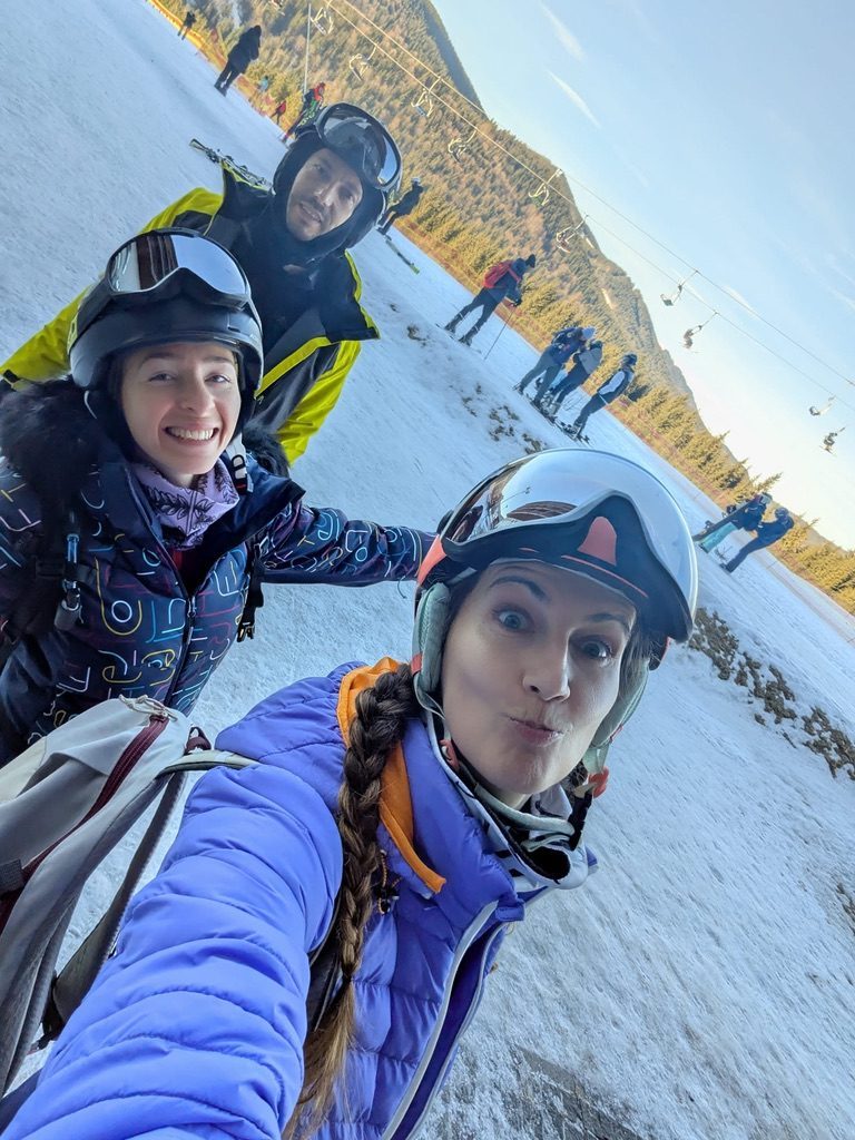 Two people on the ski slope together — friends, winter jackets, mountains behind them