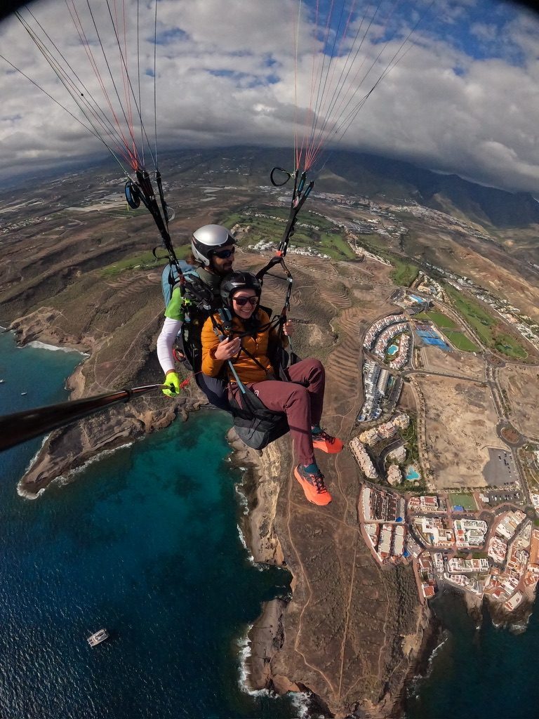 Paraglider view over the Tenerife coastline — the volcanic island seen from above, ocean on all sides, dramatic cliffs
