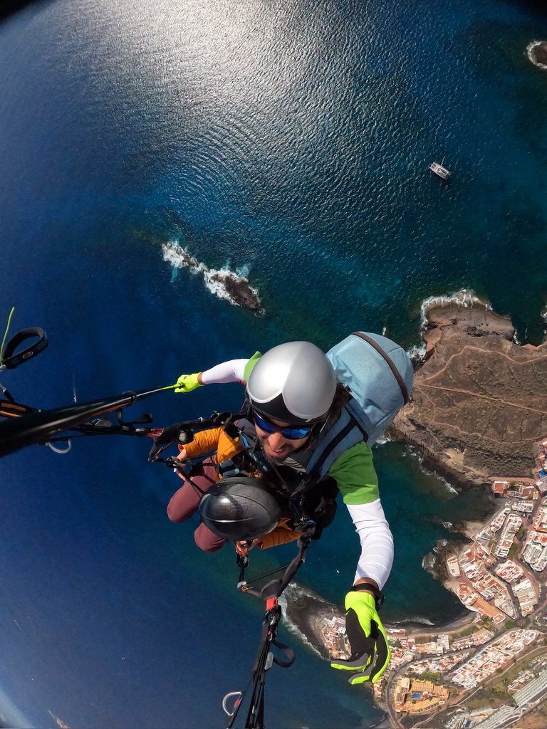Tandem paraglider airborne over Tenerife — the coast and ocean spread out below, the wing bright against the sky