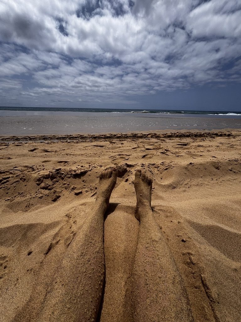 Feet buried in warm golden Porto Santo sand, ocean and cloud-covered sky beyond