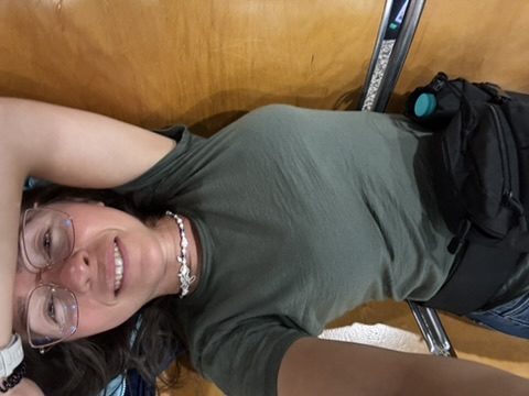 Anca lying on airport seats, glasses on, smiling, bag beside her — airport floor, waiting for the early flight