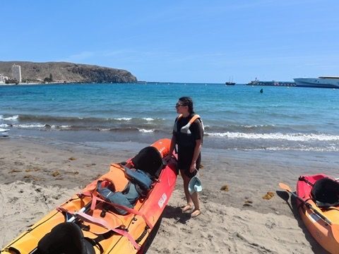 Kayaks on the water along the Tenerife coast, dramatic volcanic cliffs behind, clear turquoise sea