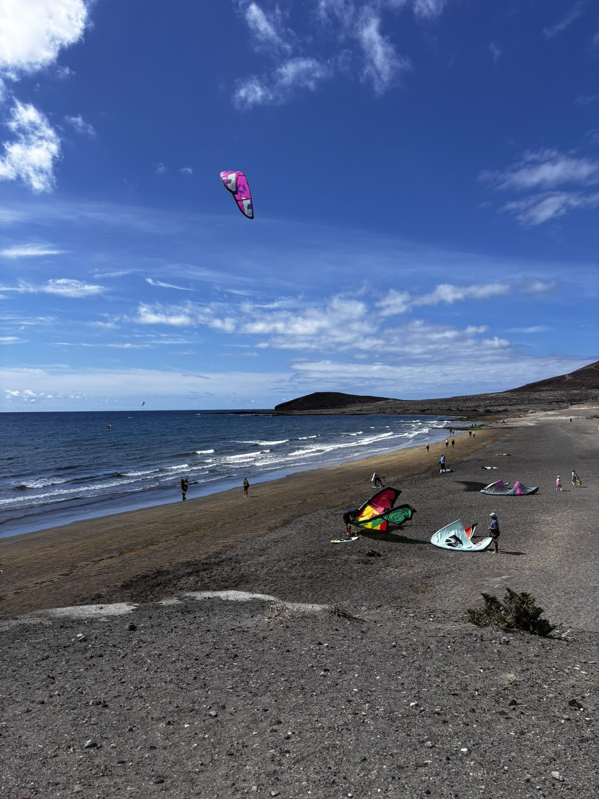 Kite surfers on a Tenerife beach, colourful kites filling the sky, wind churning the water