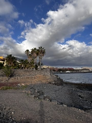 A Tenerife beach in the afternoon, golden light, people scattered, calm water