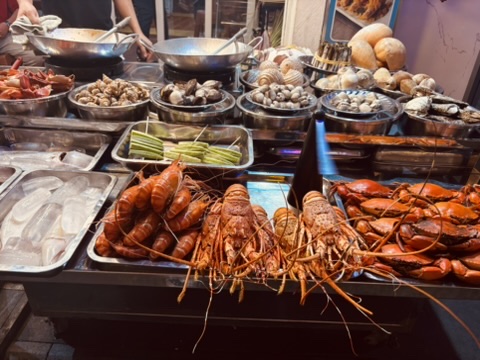 A Vietnamese night market seafood stall — whole lobsters, crayfish, clams and shellfish displayed on ice under bright lights