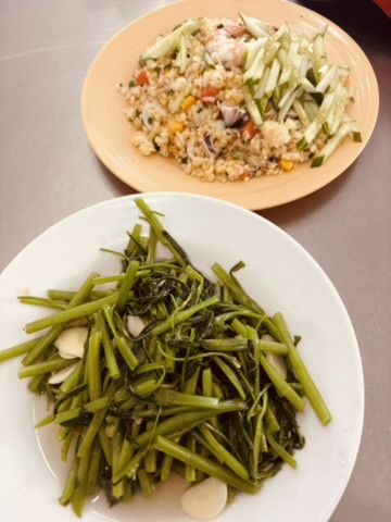 Two plates of Vietnamese food — stir-fried morning glory with garlic in the foreground, fried rice with vegetables behind