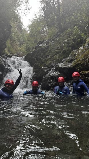 Anca fully submerged in the cascade, cold mountain water rushing around her, face turned upward