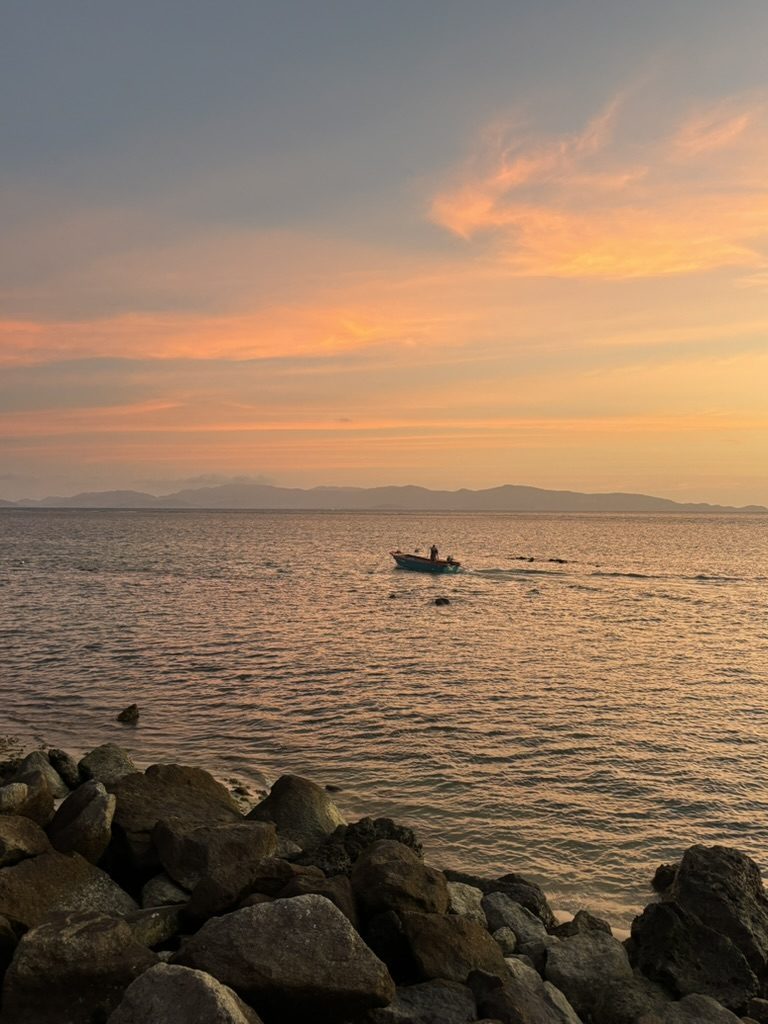 Lone fishing boat on a glassy amber sea at sunset off Koh Phangan, Thailand