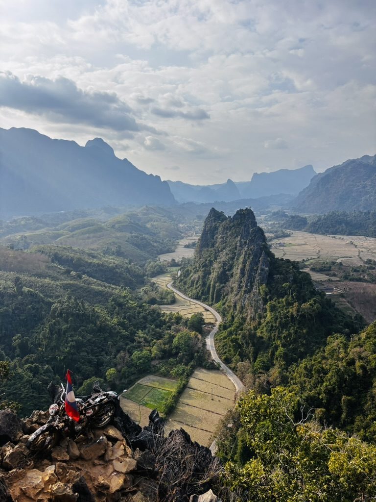Sweeping mountain valley view from a rocky summit above Vang Vieng, Laos, with a winding road below